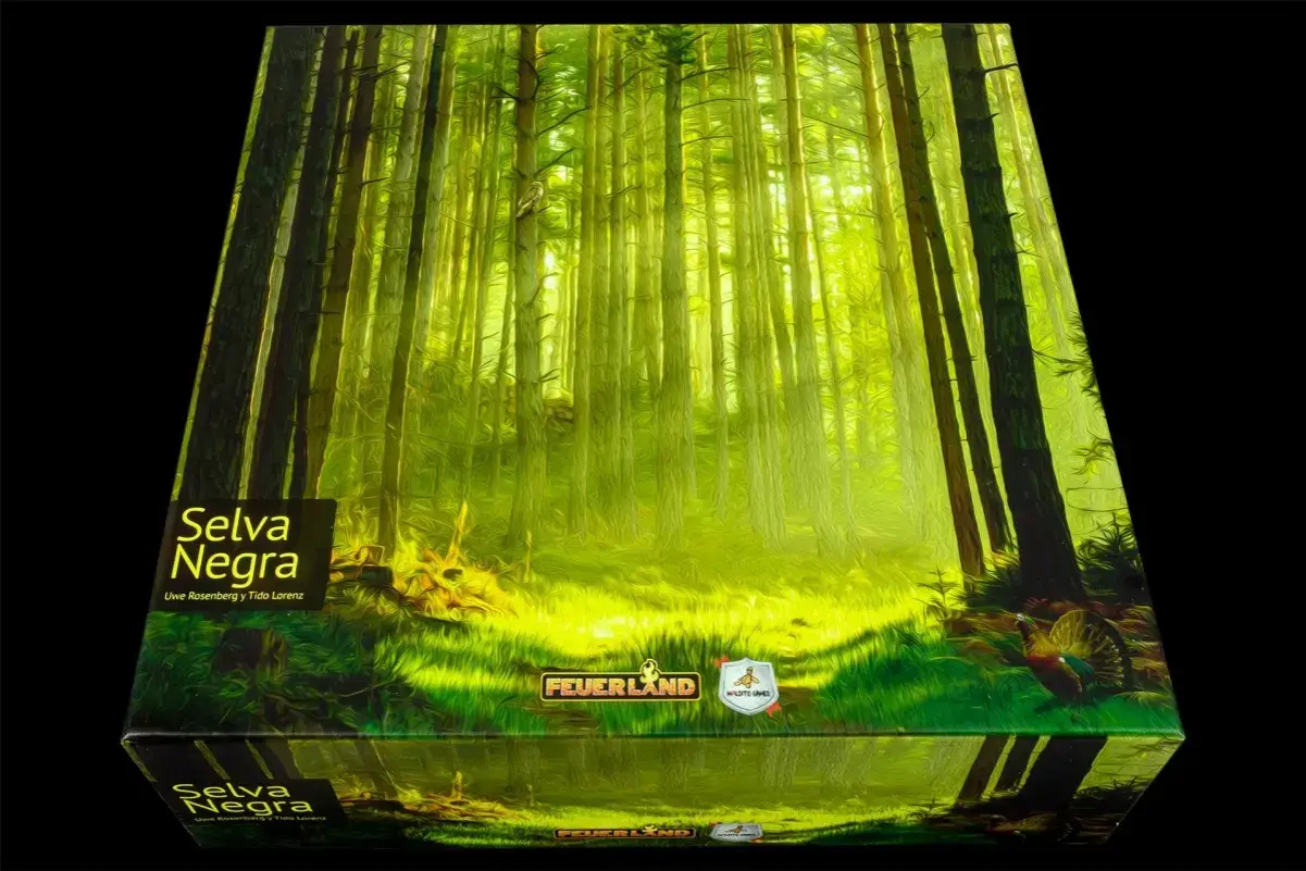 Una caja de juego con arte de bosque denso y soleado, titulada "Selva Negra". Un pavo real se asoma entre la hierba.