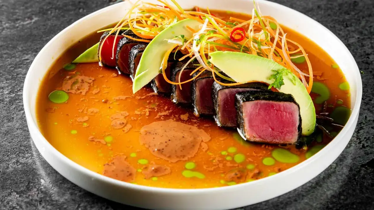 Tataki de atún sellado, servido en un caldo vibrante con aguacate, zanahoria rallada y un toque picante.