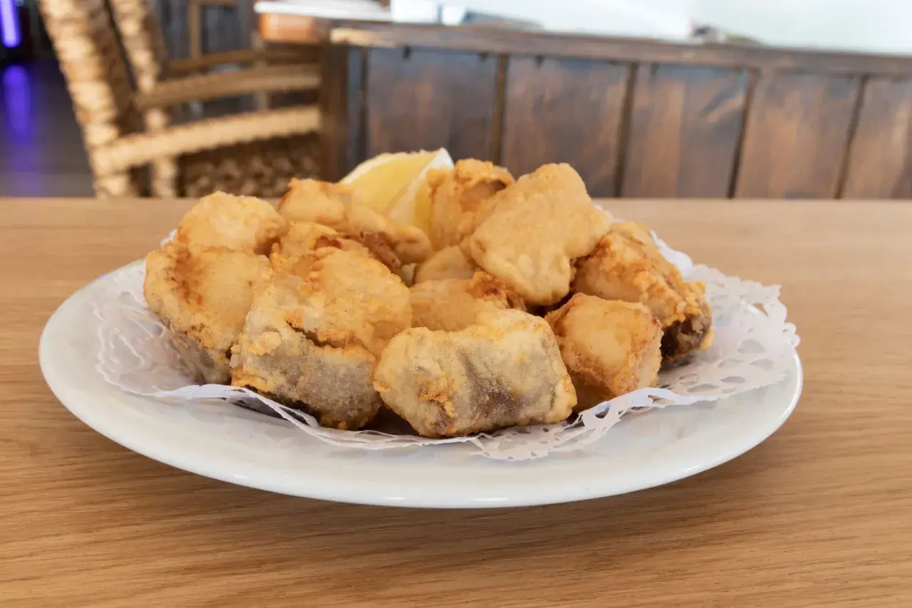 Plato de cazon en adobo, trozos de pescado frito y dorado, servido con una rodaja de limón.