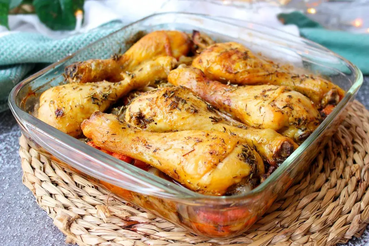 Muslos de pollo al horno dorados y jugosos, sazonados con hierbas aromáticas, servidos en una fuente de vidrio.