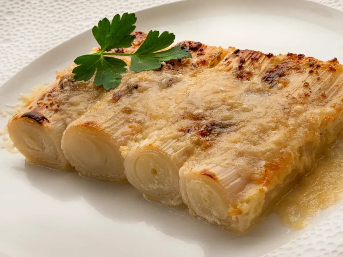 Tres tiernos puerros al horno gratinados con queso, coronados con una ramita de perejil fresco.