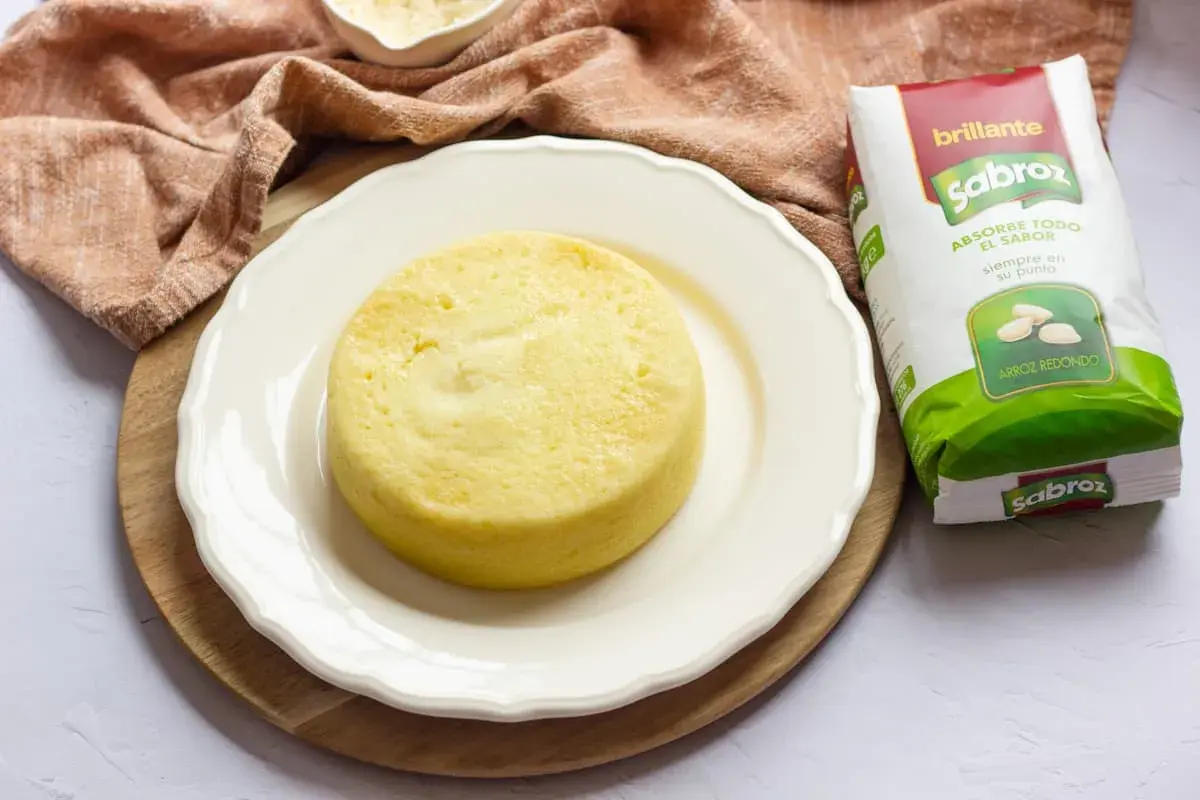 Pastel de arroz dorado y esponjoso en plato blanco, junto a un paquete de arroz Sabroz.
