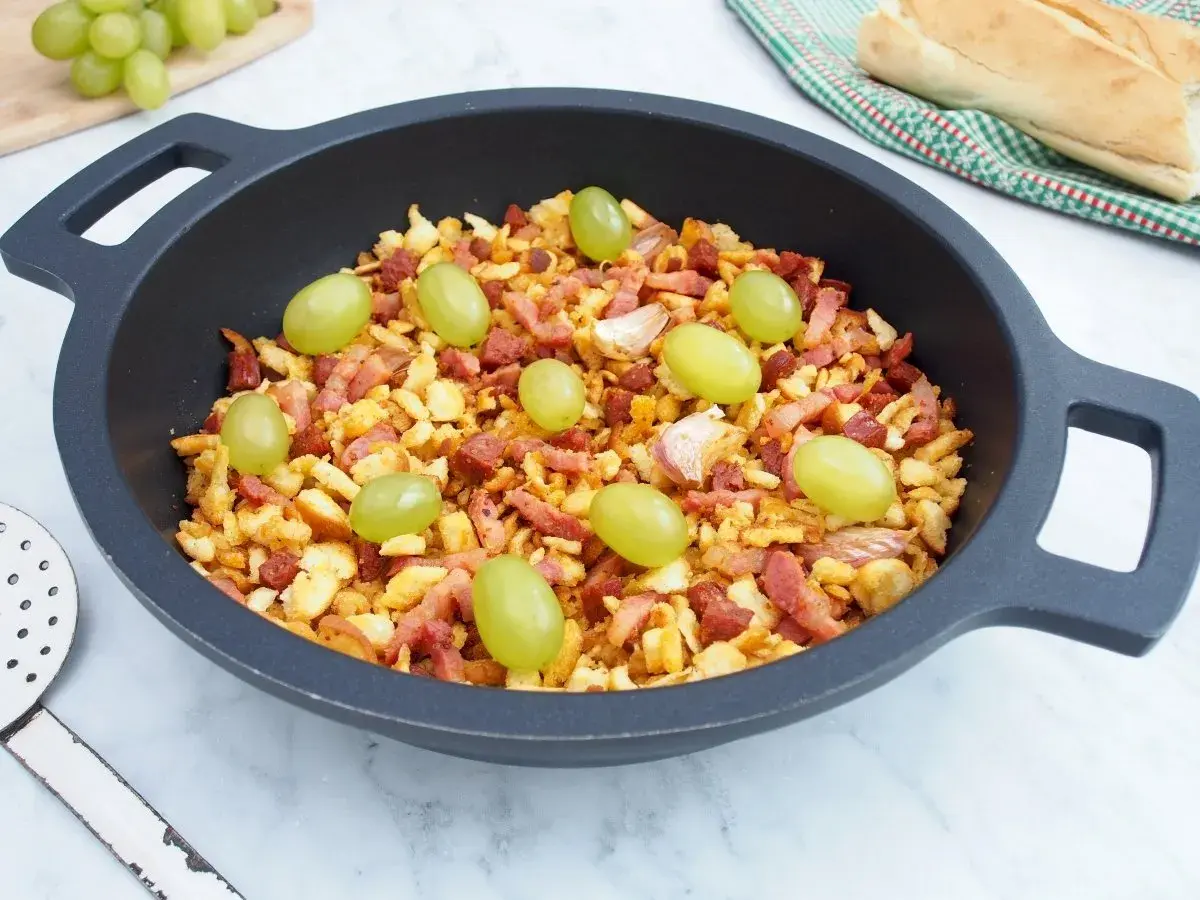 Migas manchegas con uvas verdes y ajos en una sartén. Un plato tradicional listo para disfrutar.
