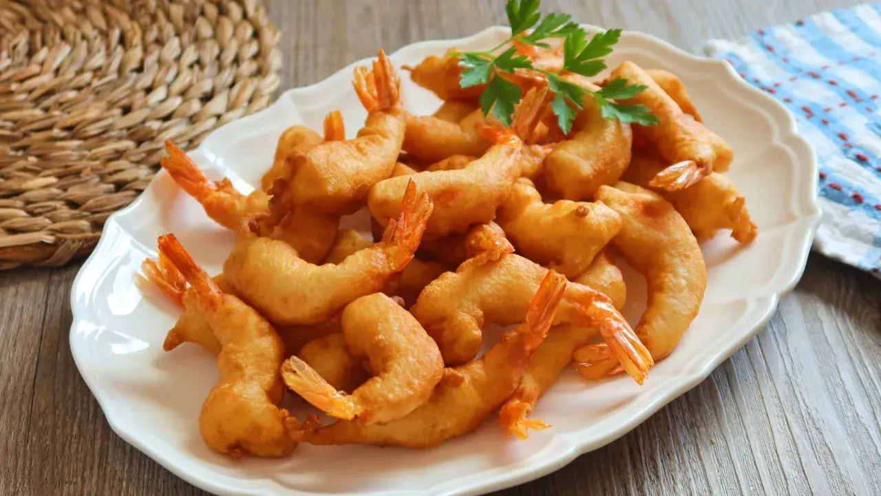 Un plato blanco lleno de gambas a la gabardina doradas y crujientes, decorado con perejil fresco.