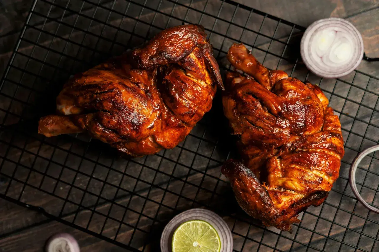 Dos jugosos pollos a la brasa, dorados y listos para disfrutar, acompañados de rodajas de cebolla roja y limón.
