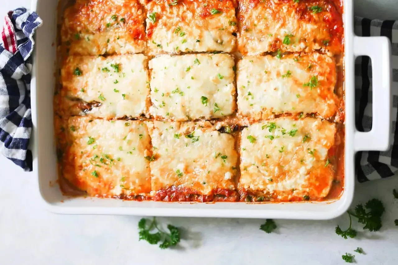 Una deliciosa lasaña de berenjena recién horneada, cubierta de queso derretido y perejil picado, lista para servir.