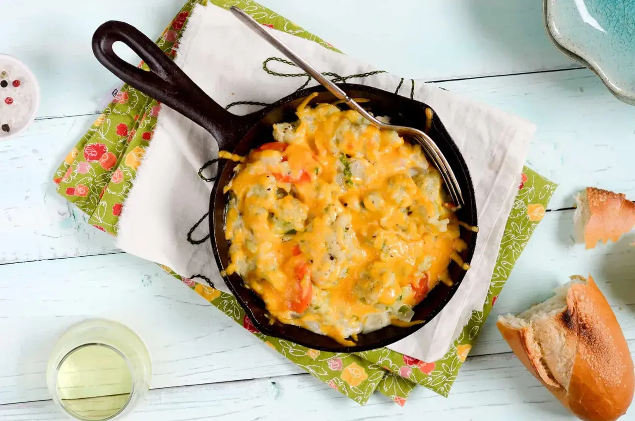 Coliflor gratinada burbujeante en sartén de hierro fundido, lista para disfrutar con pan crujiente.