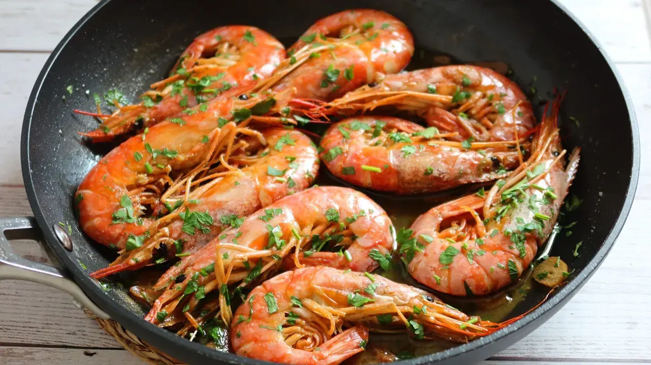 Gambones al ajillo chisporroteando en una sartén, con perejil fresco espolvoreado. ¡Un plato delicioso!