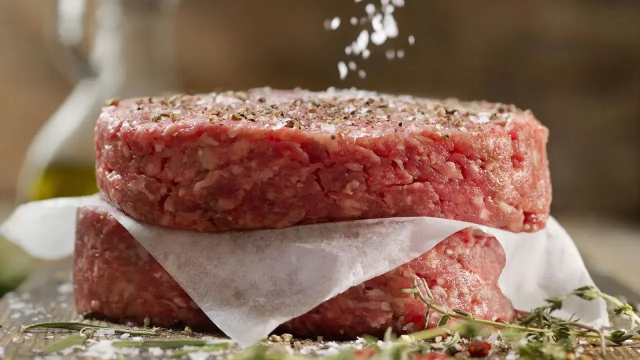 Dos hamburguesas de carne picada apiladas, sazonadas con sal y pimienta.