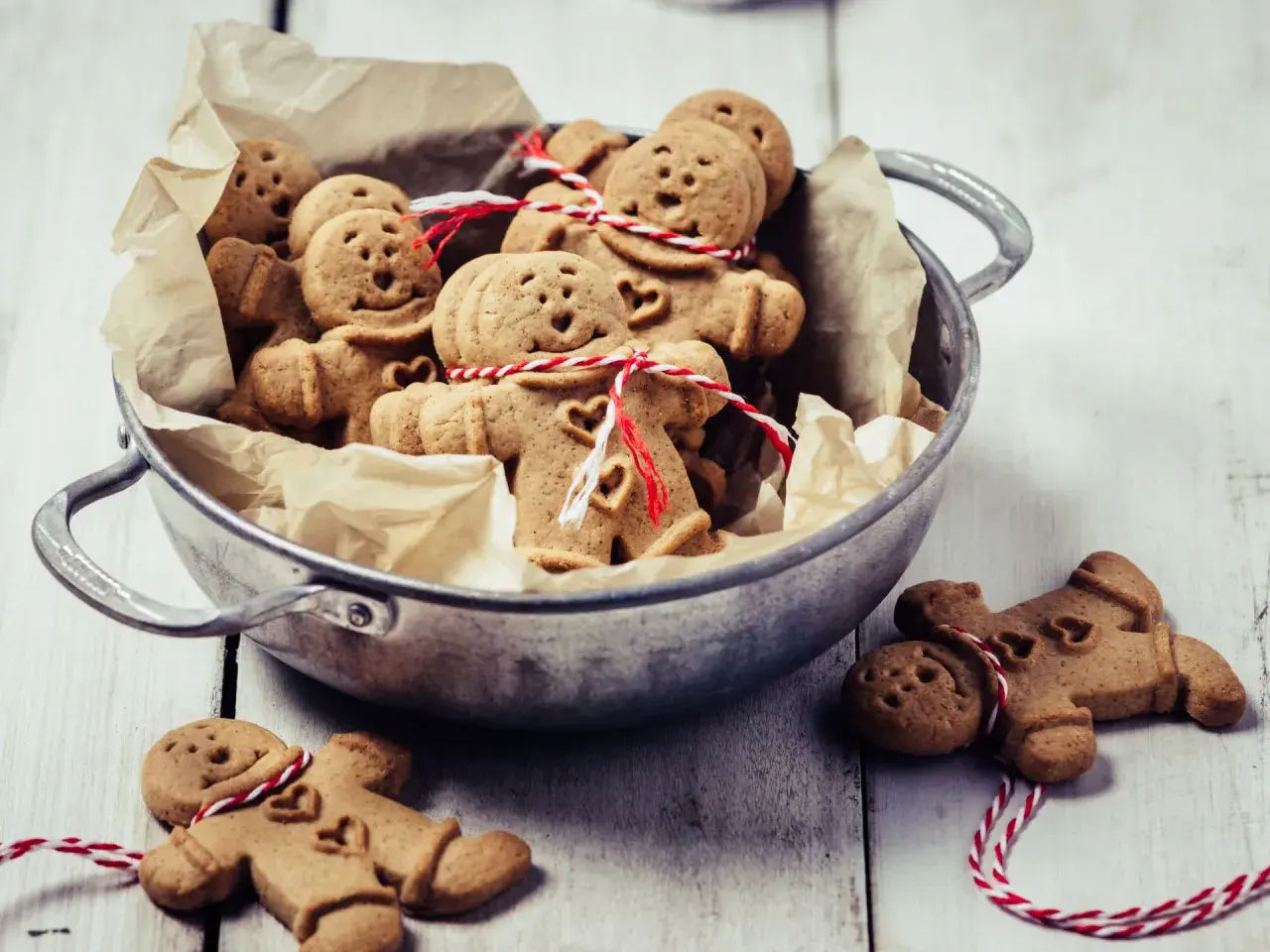 Un cuenco lleno de galletas de jengibre con forma de hombrecito, algunas atadas con hilo rojo y blanco.