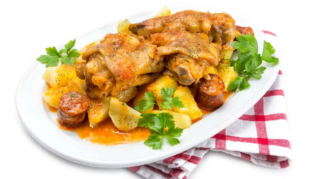 Manitas de cerdo guisadas con patatas y chorizo, decoradas con perejil fresco. Un plato tradicional y sabroso.