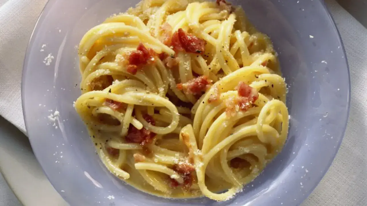 Un plato de pasta carbonara cremoso con trozos de panceta crujiente y espolvoreado con queso rallado.