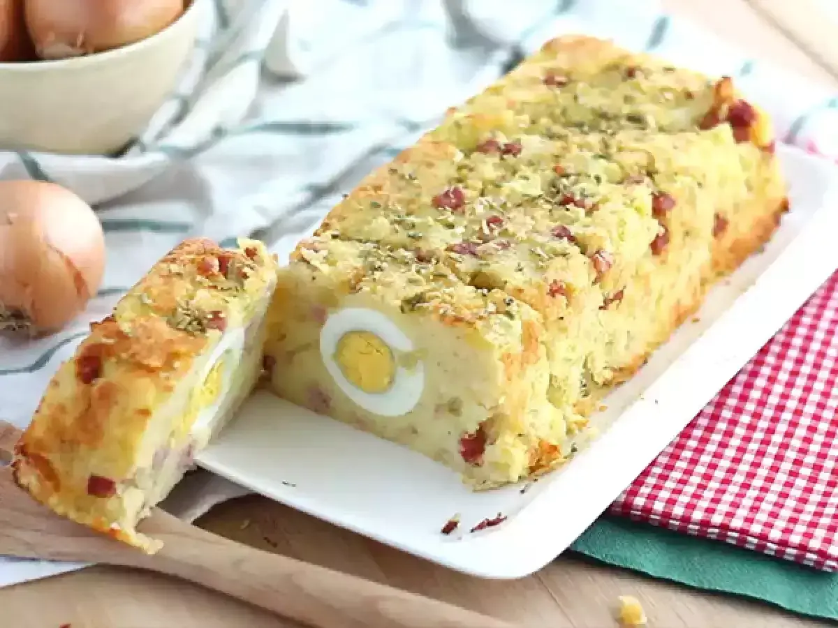 Un delicioso pastel de patata con trozos de bacon y huevos duros en su interior, espolvoreado con hierbas.