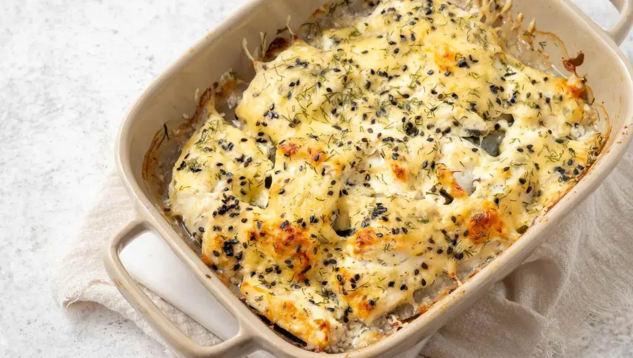 Bacalao a la nata gratinado, cubierto con semillas negras y eneldo, burbujeando en una fuente de cerámica.