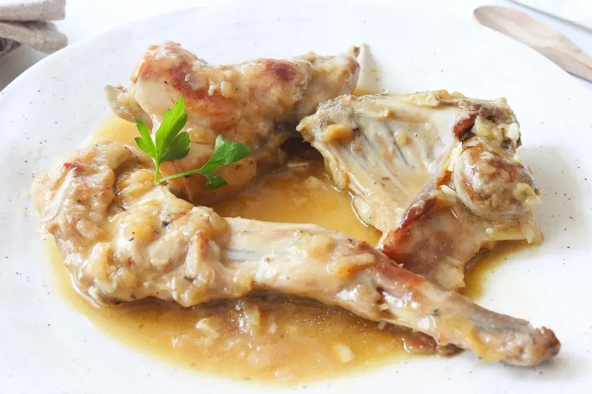 Deliciosas recetas de conejo guisado en salsa, servido en plato blanco con perejil fresco.