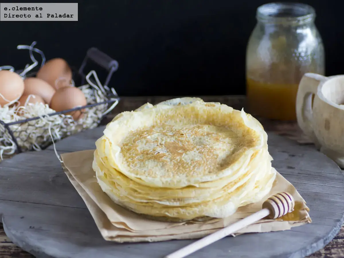 Pila de filloas gallegas recién hechas, con miel en un tarro y huevos en una cesta al fondo.