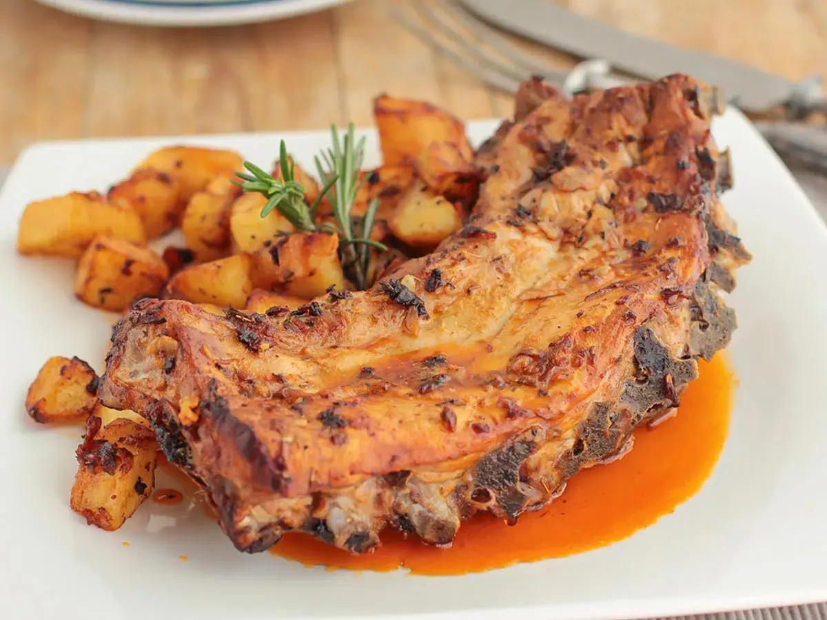 Costillas al horno con patatas doradas y romero fresco. Un plato jugoso y apetitoso.