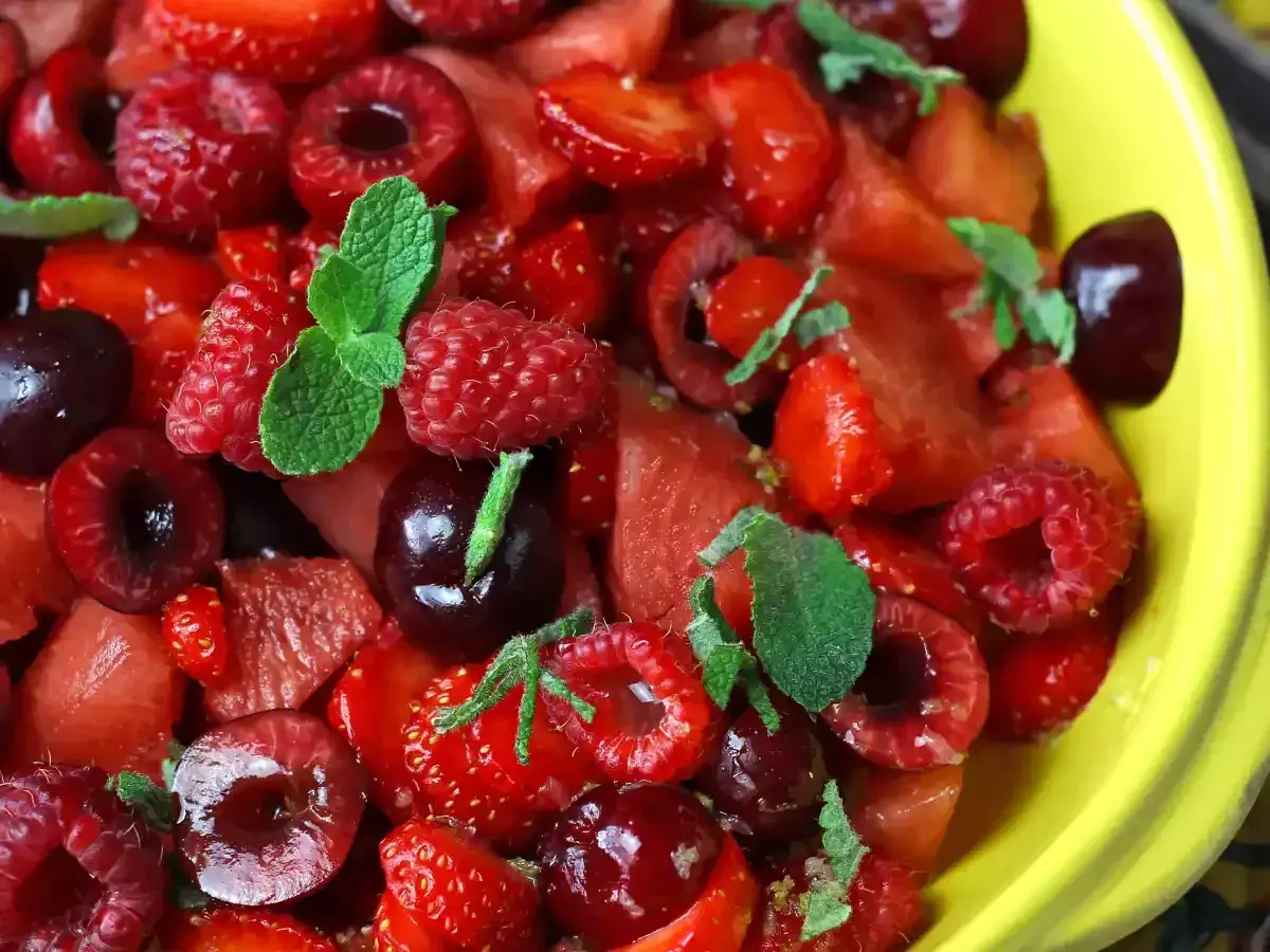 Delicioso postre con fresas, frambuesas, cerezas y menta en un tazón amarillo.