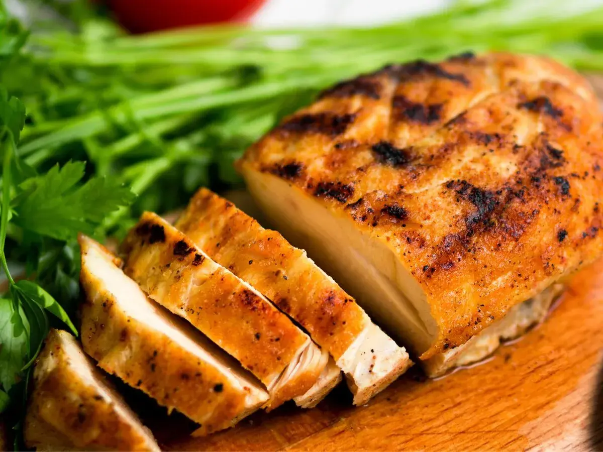 Pechuga de pollo a la parrilla, jugosa y dorada, lista para ser parte de tus recetas con pechuga de pollo. Acompañada de perejil fresco.
