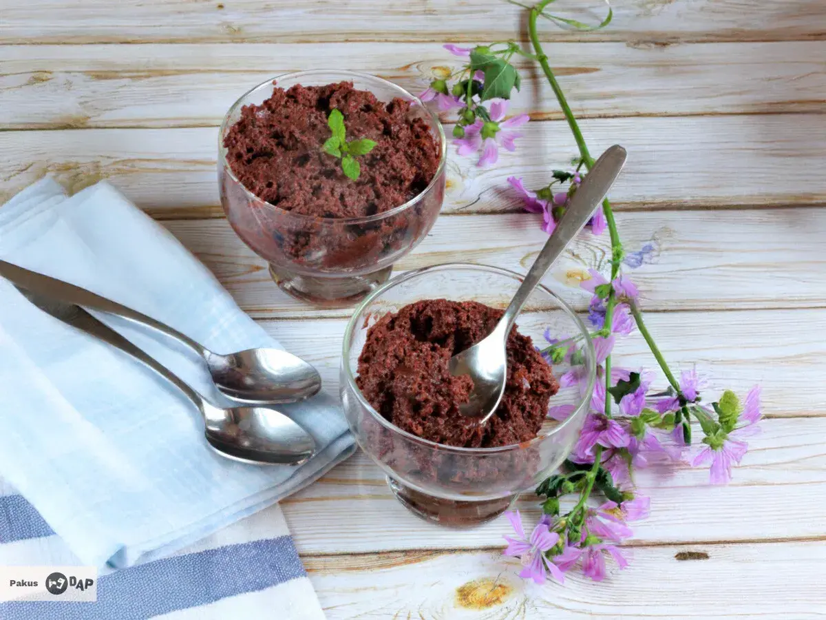 Dos copas de delicioso mousse de chocolate, decoradas con menta y flores moradas, listas para disfrutar.