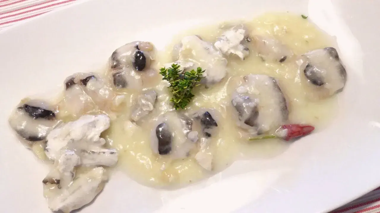 Deliciosas cocochas de merluza en salsa cremosa, adornadas con una ramita de tomillo y un toque de pimiento rojo.
