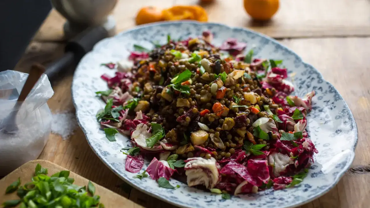 Deliciosa ensalada de lentejas con verduras crujientes y radicchio morado, servida en un plato decorado.