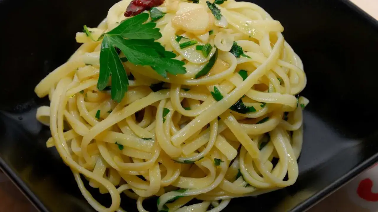 Un plato de pasta al ajillo con perejil fresco, ajo laminado y un toque de guindilla.