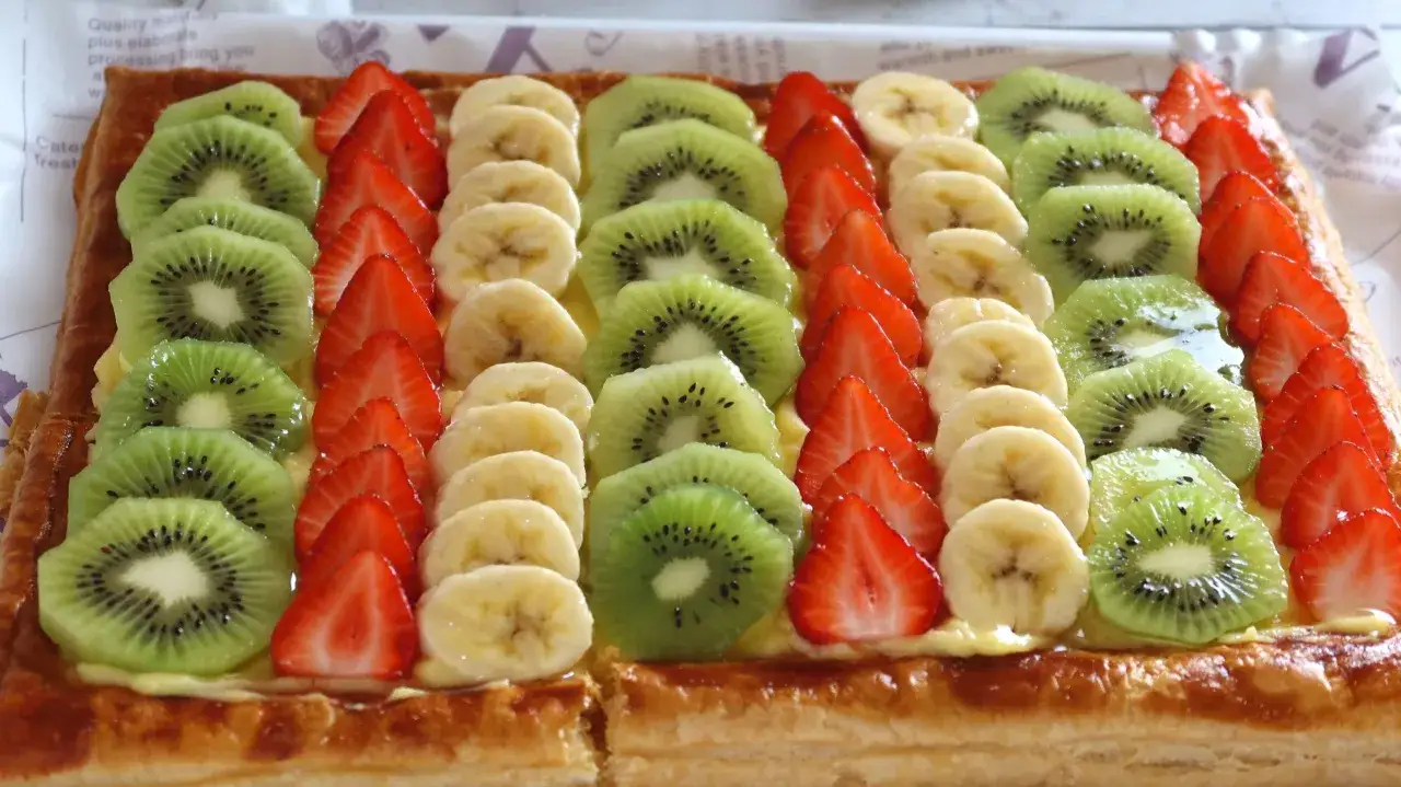 Delicioso postre con hojaldre, cubierto con crema y filas de fresas, rodajas de plátano y kiwi.