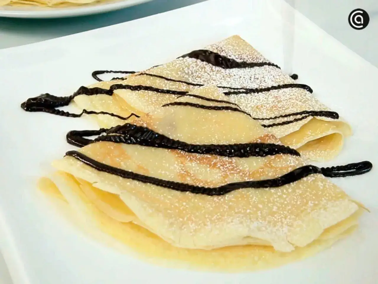 Deliciosos crepes doblados, espolvoreados con azúcar glas y cubiertos con sirope de chocolate. Una receta fácil y rápida.