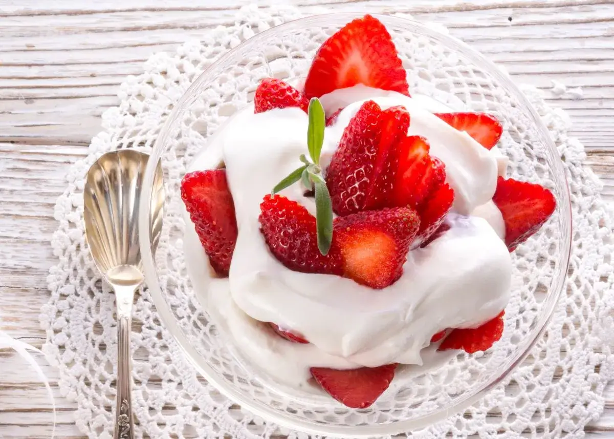 Fresas frescas con abundante nata montada en un cuenco de cristal, servidas con una cuchara plateada sobre un mantel de encaje.