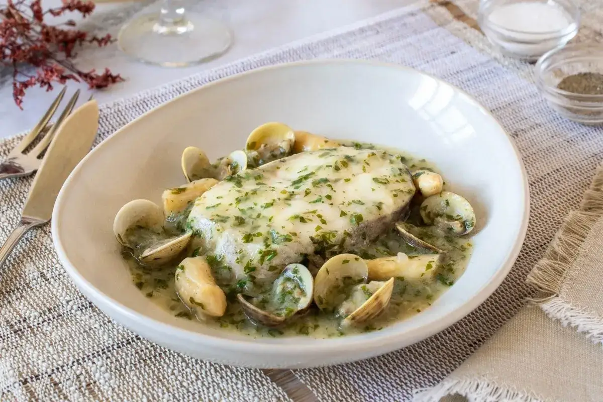 Delicioso pescado en salsa verde con almejas, servido en un plato blanco.