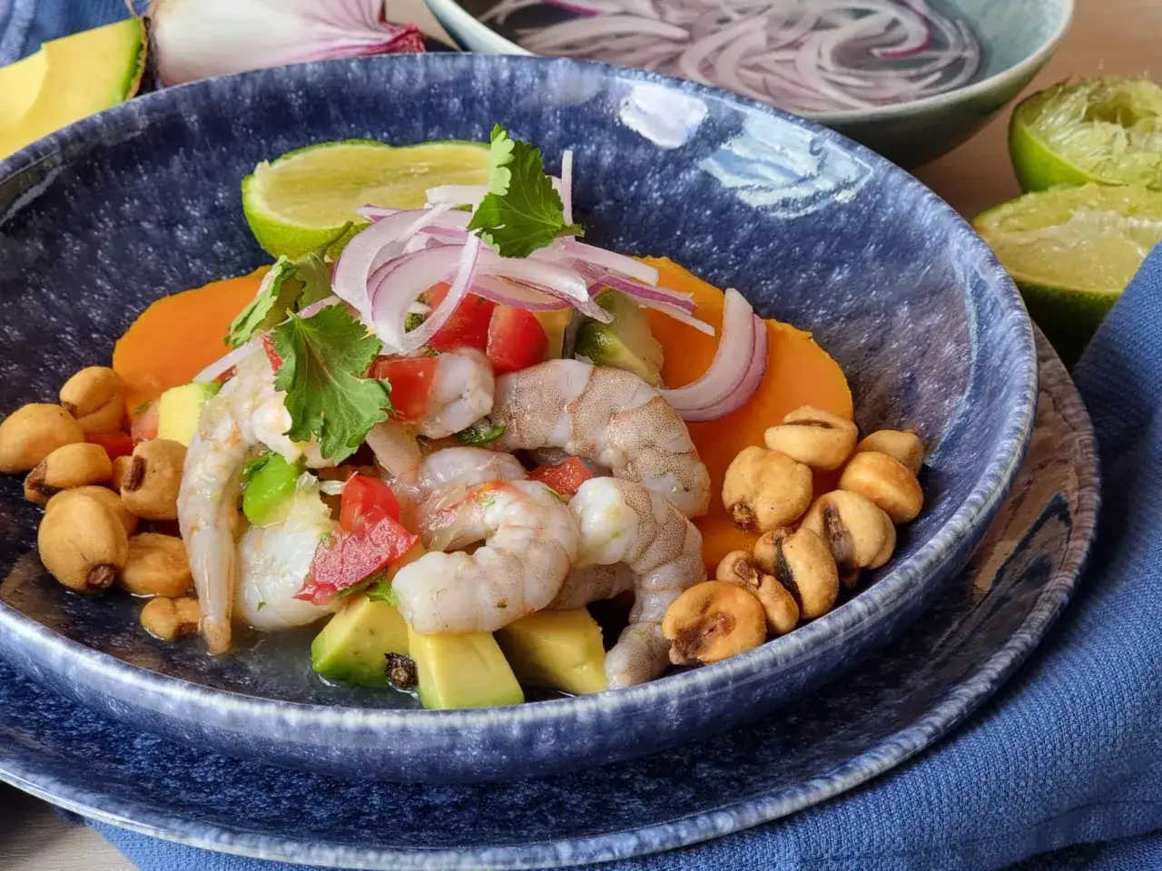 Delicioso ceviche de gambas con aguacate, tomate, cebolla morada, camote y cancha serrana en un tazón azul.