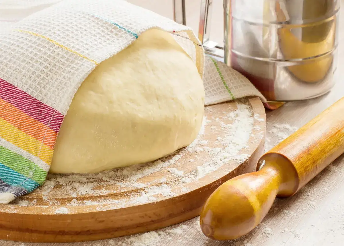 Masa de pan casero reposando, lista para amasar. Rodillo y harina esparcida, ingredientes para como hacer pan en casa.