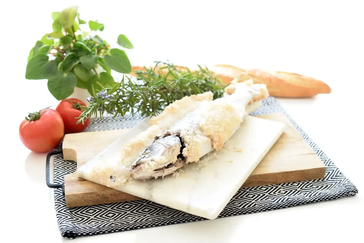 Lubina a la sal lista para servir, acompa&ntilde;ada de tomates frescos, romero y pan r&uacute;stico.