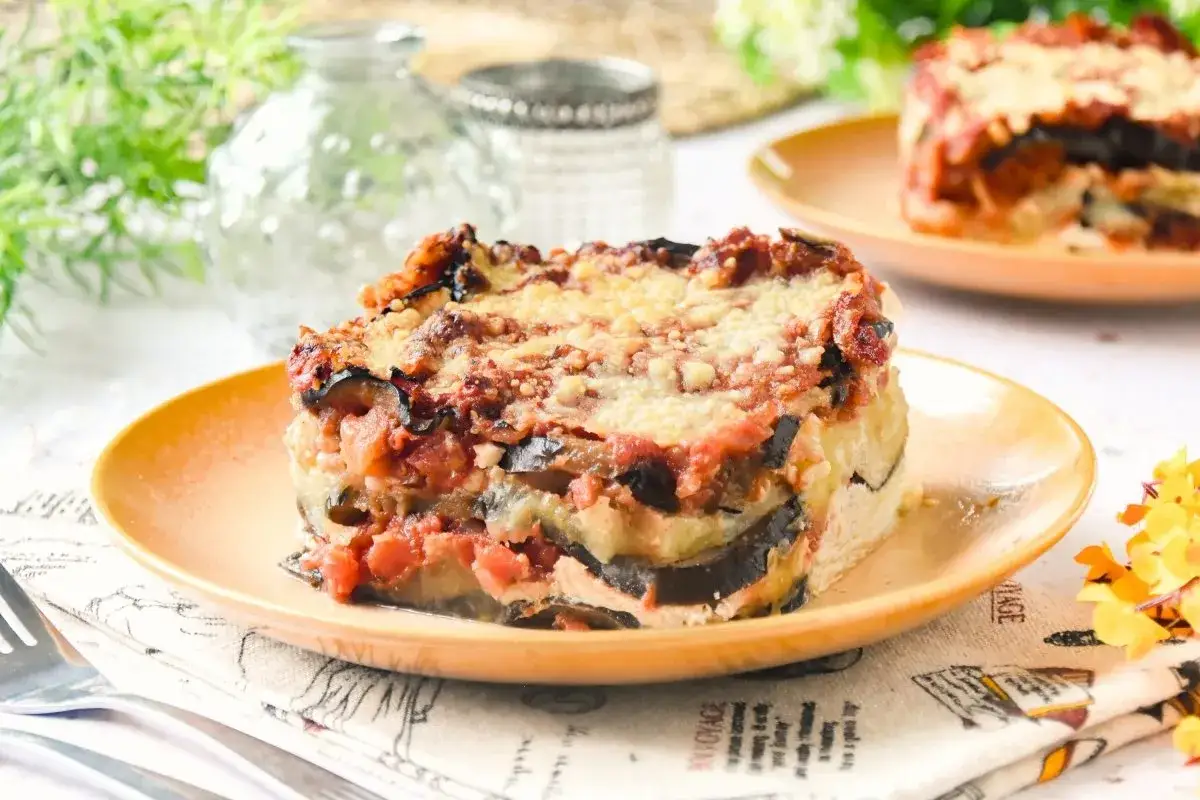 Porción de lasaña de berenjena horneada, con capas de berenjena, salsa de tomate y queso gratinado, servida en plato naranja.