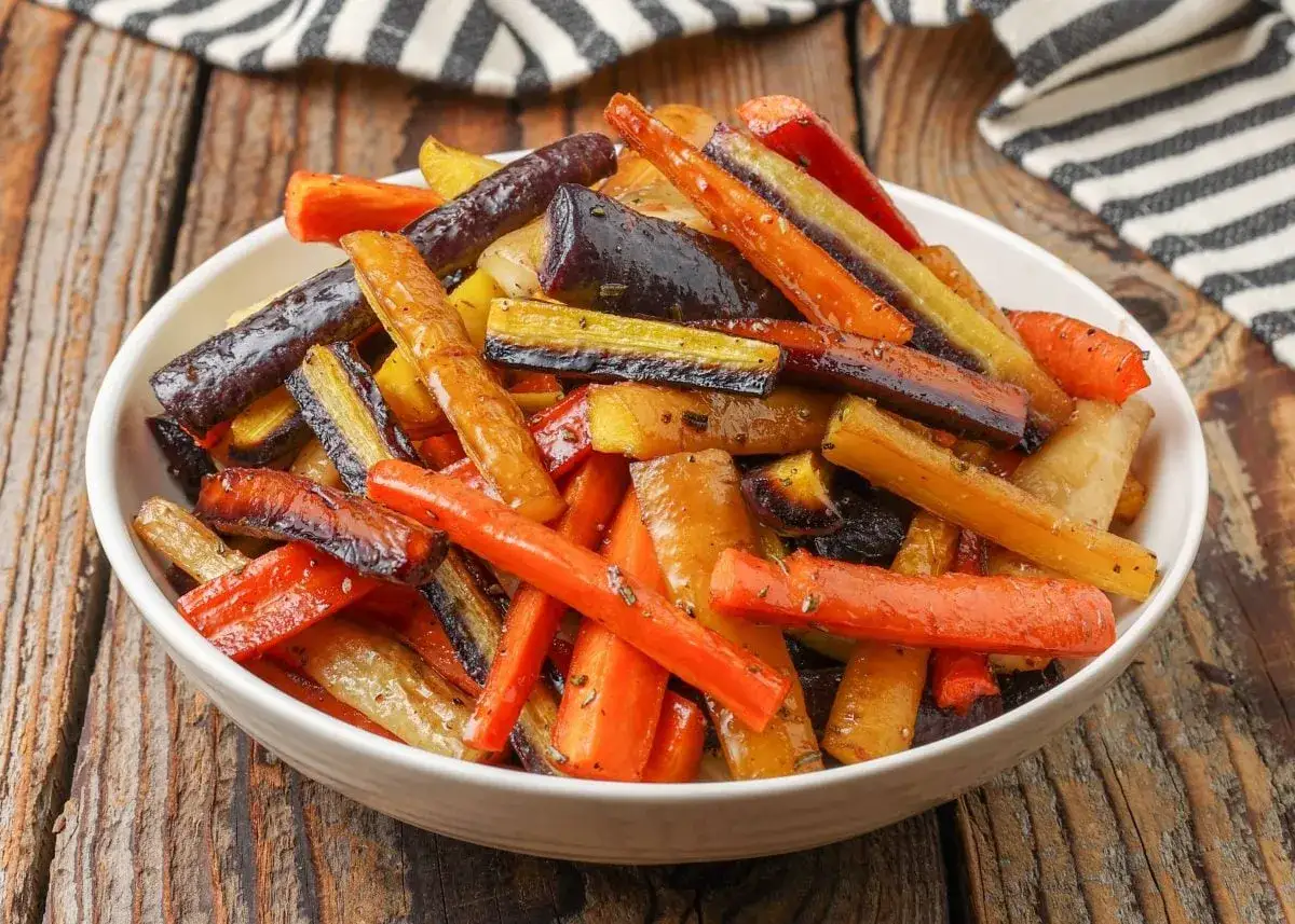 Un tazón blanco lleno de zanahorias asadas de colores vibrantes, perfectas para tus recetas con zanahoria.