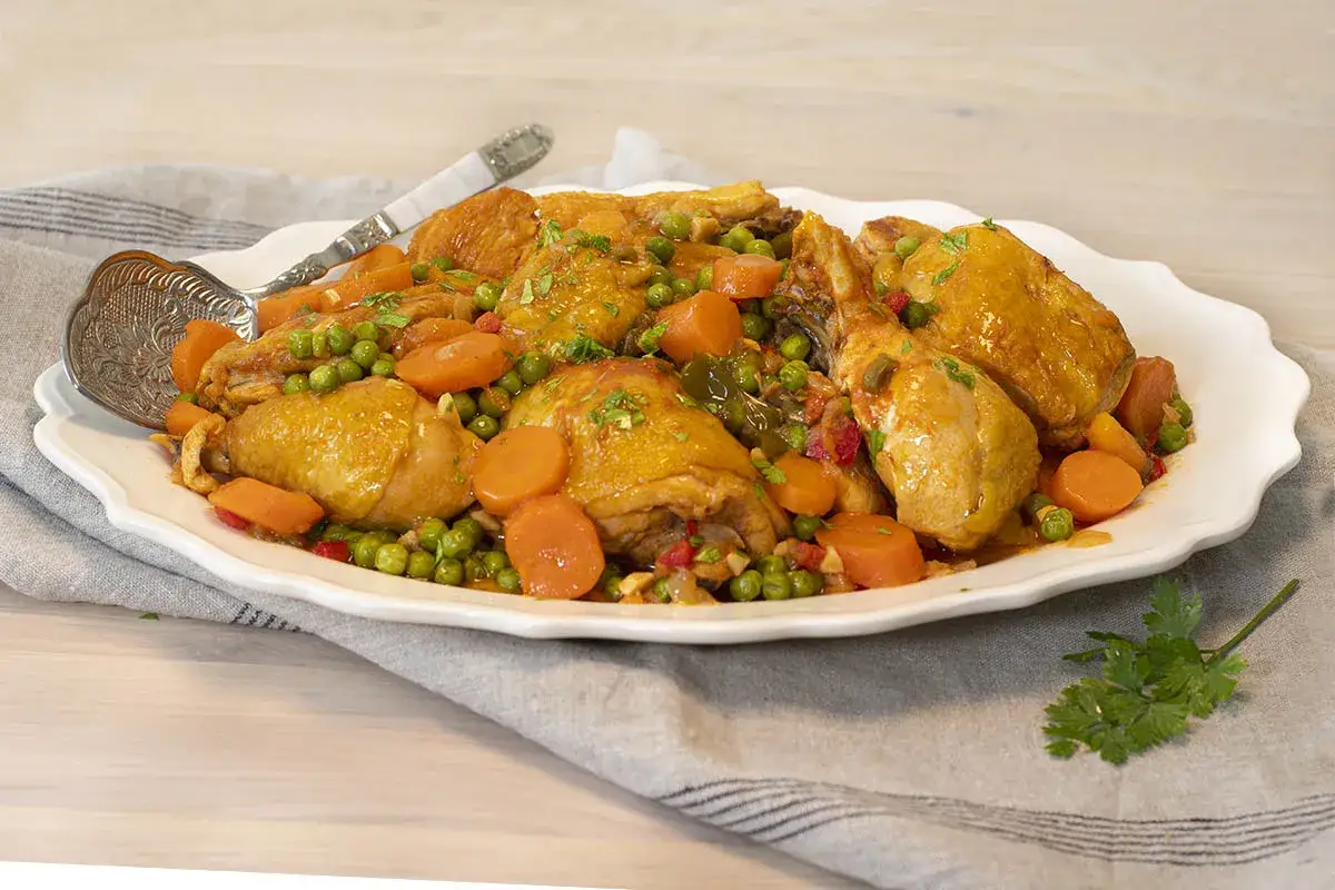 Delicioso estofado de pollo con zanahorias y guisantes, servido en una fuente blanca con una cuchara de plata.