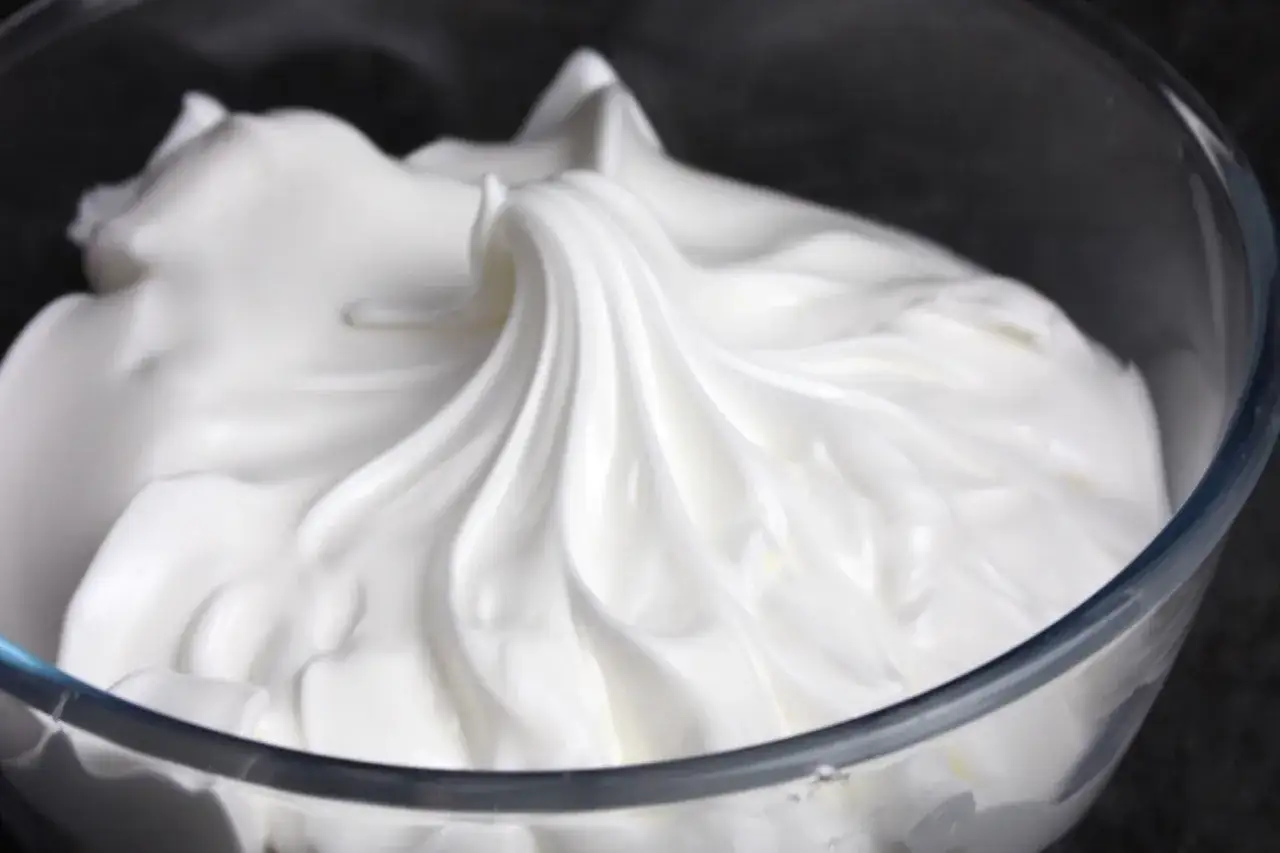 Merengue italiano esponjoso y brillante en un bol de cristal, listo para decorar postres.