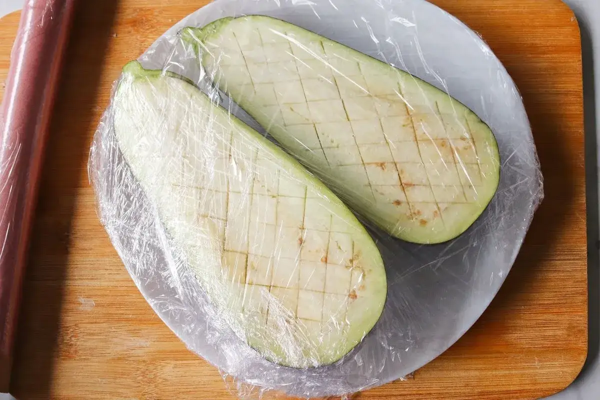 Berenjenas cortadas y cubiertas con film transparente, listas para cocinar al microondas.