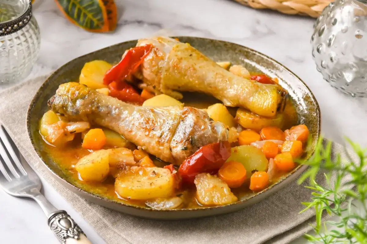 Dos muslos de pollo guisado con patatas, zanahorias y pimientos rojos en una salsa sabrosa.