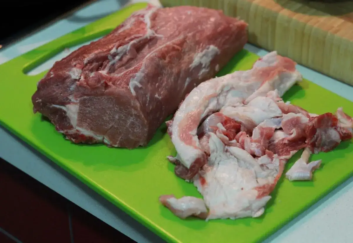 Un trozo de raxo gallego crudo y grasa de cerdo sobre una tabla de cortar verde, listo para cocinar.