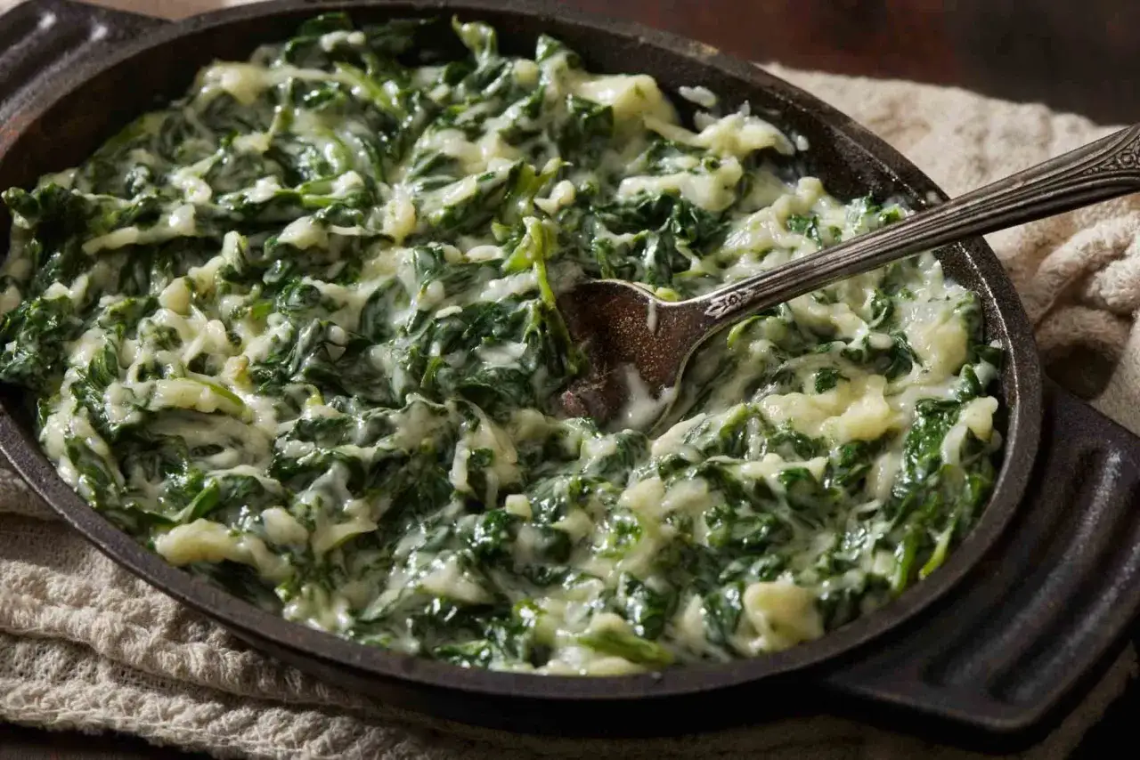 Cremosas espinacas a la crema servidas en una sartén de hierro fundido, con una cuchara lista para servir.