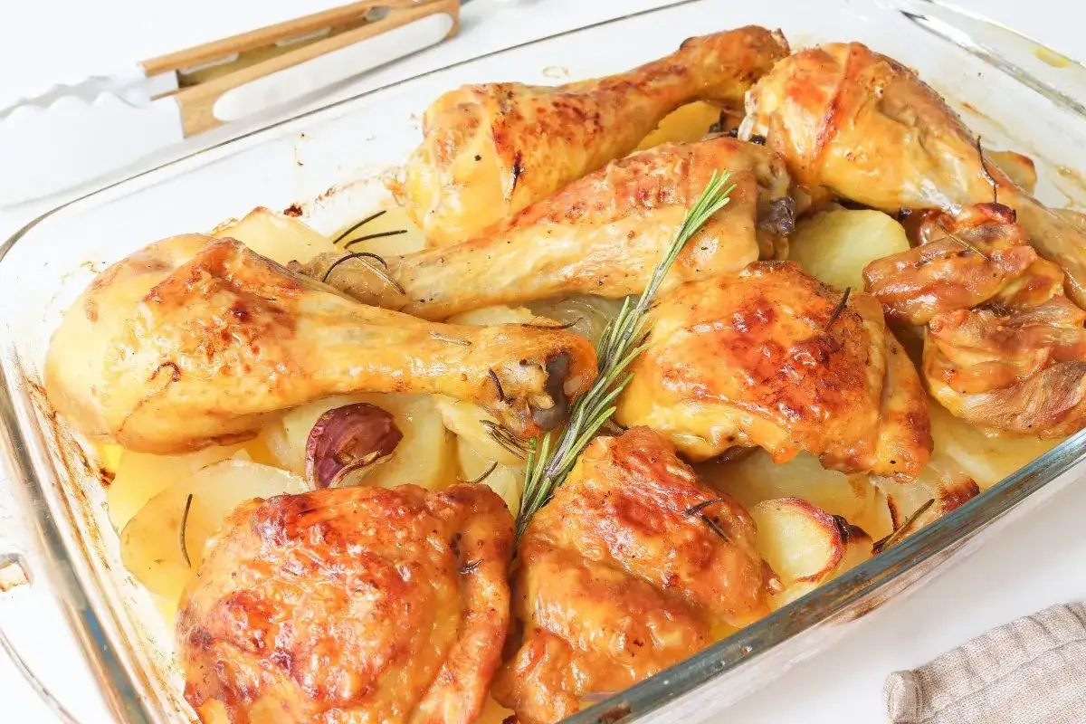Pollo al horno dorado y jugoso, acompa&ntilde;ado de patatas, ajo y romero en una bandeja de cristal. &iexcl;Un fest&iacute;n listo para servir!