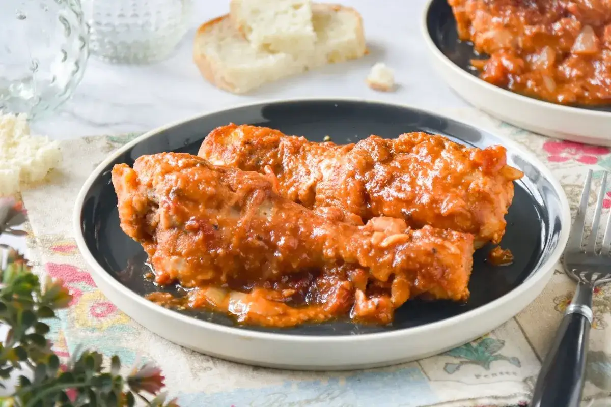 Jamoncitos de pollo en salsa, servidos en plato oscuro, acompañados de pan y tenedor.