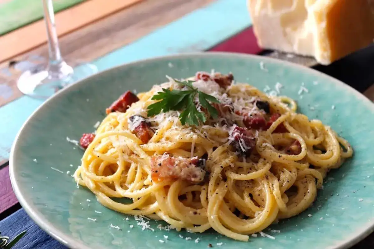 Un plato de pasta carbonara cremoso, adornado con perejil fresco y queso rallado, con trozos de panceta crujiente.