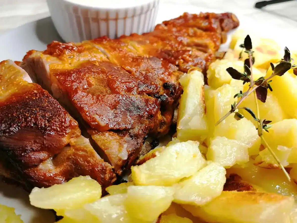 Costillas a la barbacoa jugosas y doradas, acompa&ntilde;adas de patatas asadas y una ramita de romero. &iexcl;Un fest&iacute;n para los sentidos!