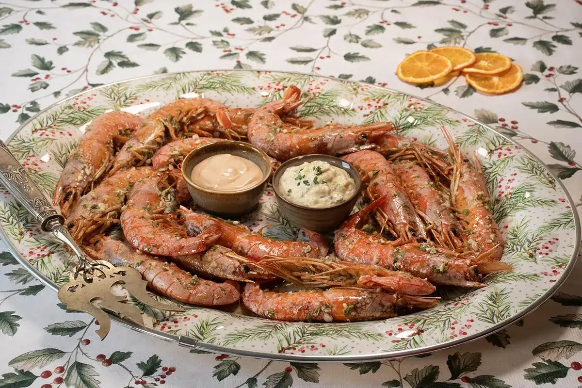 Plato festivo de gambones al horno, servidos con dos salsas y decorado con rodajas de naranja.