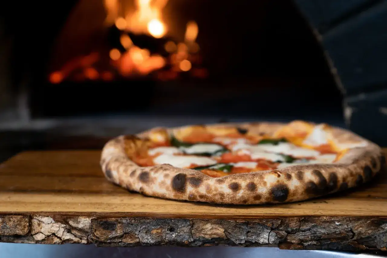 Pizza casera recién salida del horno de leña, con su masa dorada y burbujeante, lista para ser disfrutada.