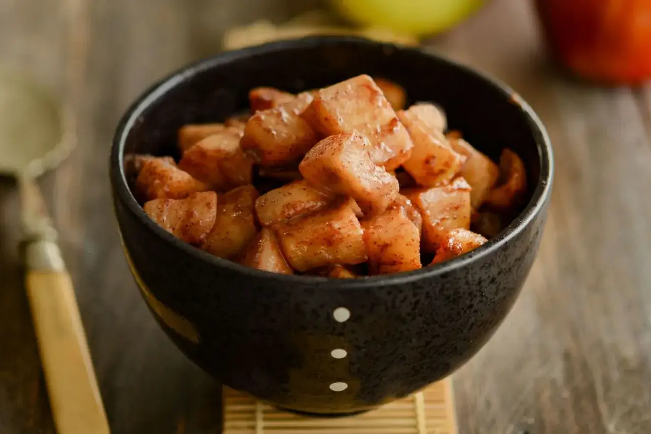 Trozos de compota de manzana especiada, servidos en un cuenco oscuro.