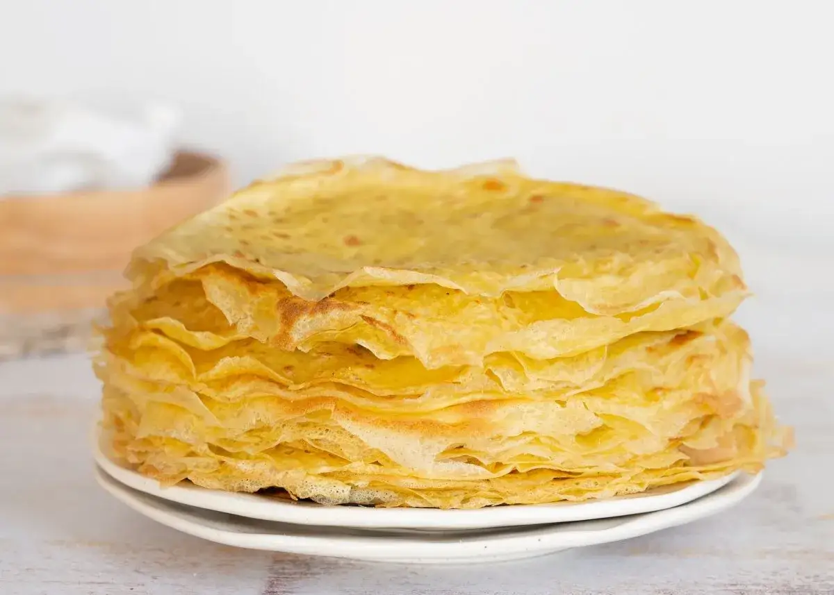 Una pila alta de filloas gallegas doradas y finas, apiladas en un plato blanco.